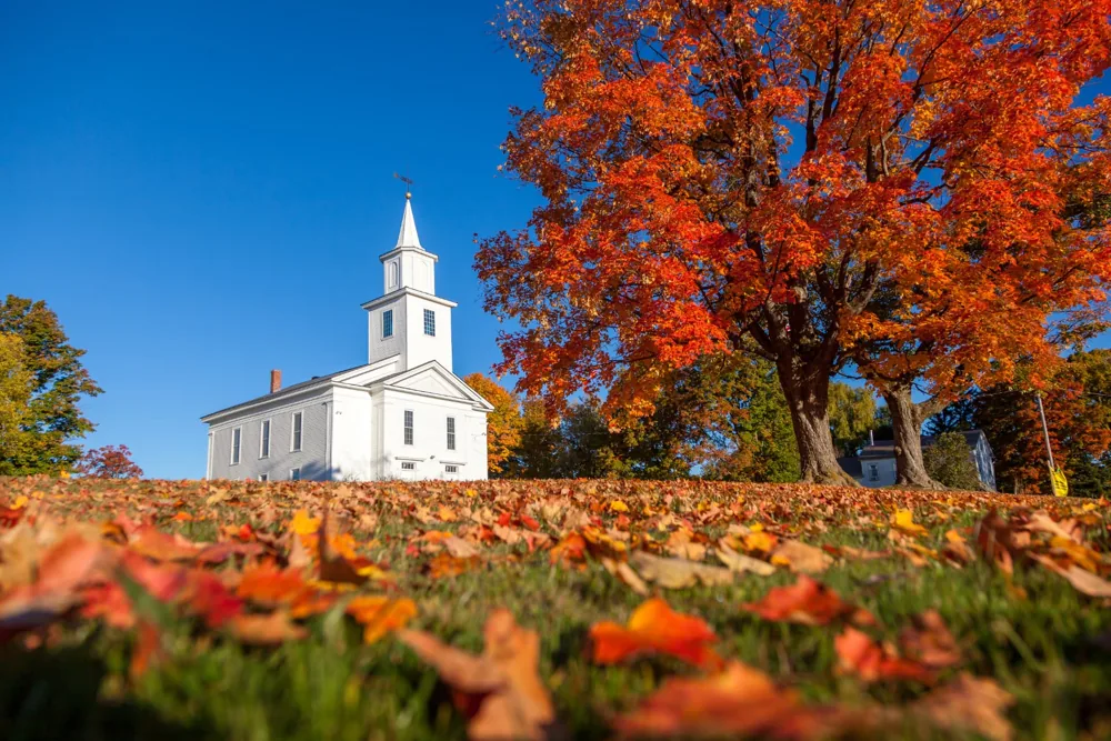New England autumn landscape with a white steepled building and orange foliage