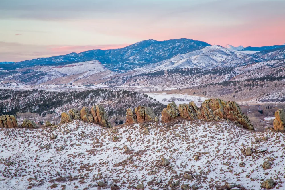 Snow-covered Colorado Rocky Mountain foothills beneath a pink evening sky